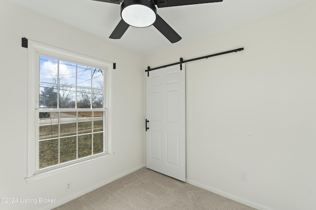 carpeted empty room featuring a barn door and ceiling fan