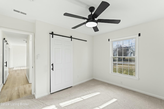 unfurnished bedroom with ceiling fan, a barn door, and light carpet