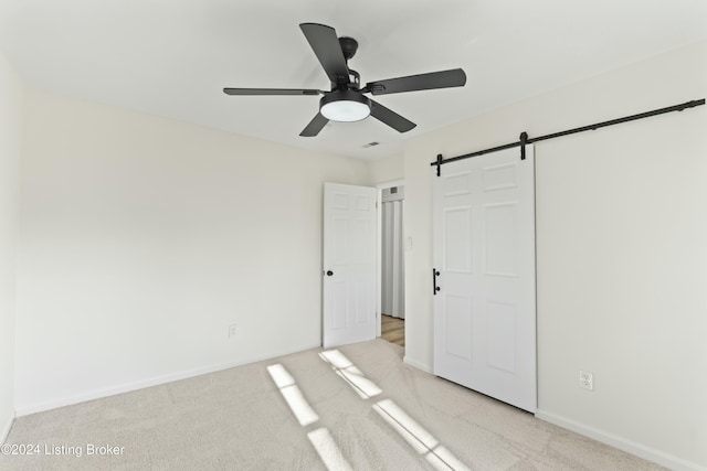 unfurnished bedroom featuring ceiling fan, a barn door, and light colored carpet