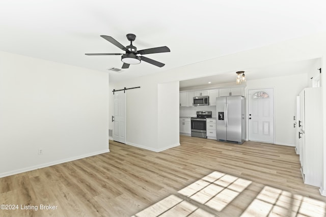 unfurnished living room with a barn door, ceiling fan, and light hardwood / wood-style flooring