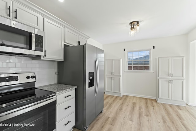 kitchen with backsplash, light stone counters, stainless steel appliances, light hardwood / wood-style floors, and white cabinetry