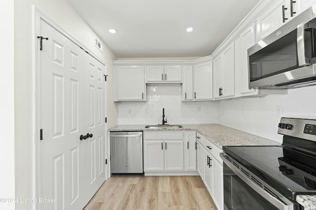 kitchen with white cabinets, appliances with stainless steel finishes, light stone countertops, and sink