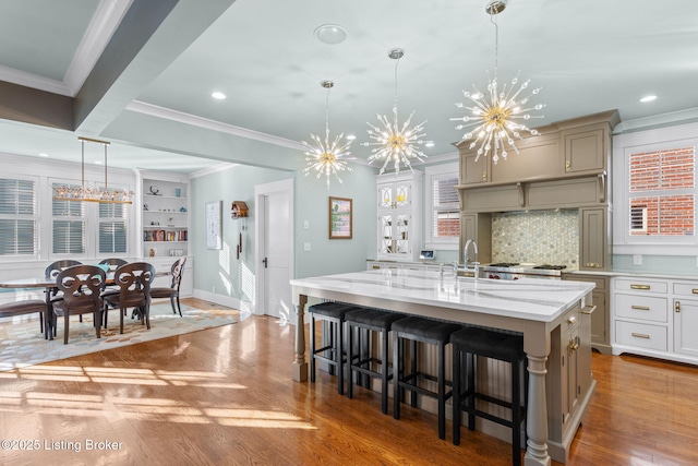 kitchen featuring a large island with sink, crown molding, light hardwood / wood-style floors, and decorative light fixtures