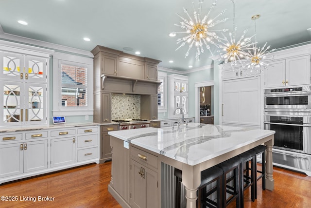 kitchen featuring a large island, hanging light fixtures, double oven, a kitchen breakfast bar, and wood-type flooring