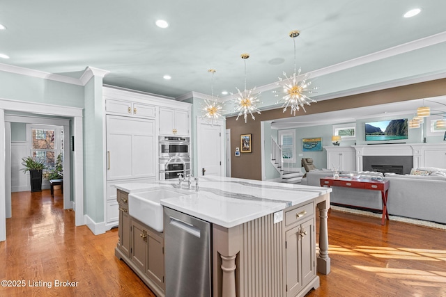 kitchen with crown molding, stainless steel appliances, decorative light fixtures, and a kitchen island with sink