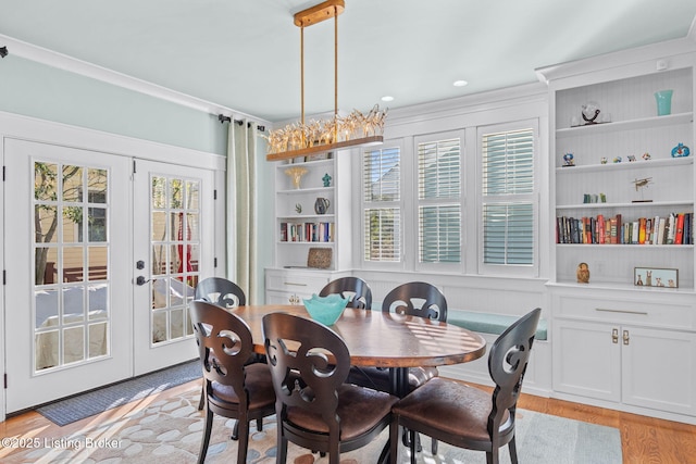 dining space with french doors, crown molding, built in shelves, and light hardwood / wood-style flooring