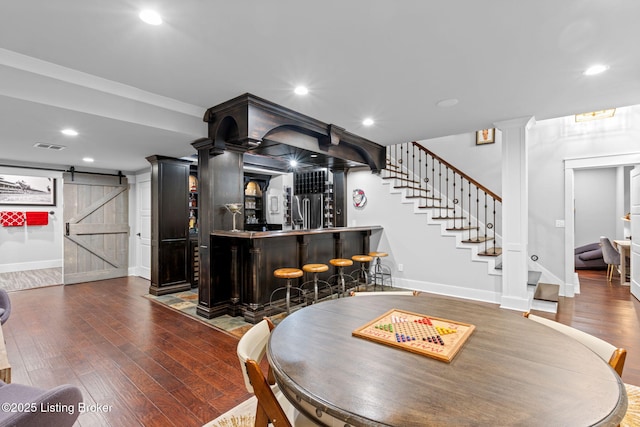 dining space with dark hardwood / wood-style floors, a barn door, ornate columns, and bar area