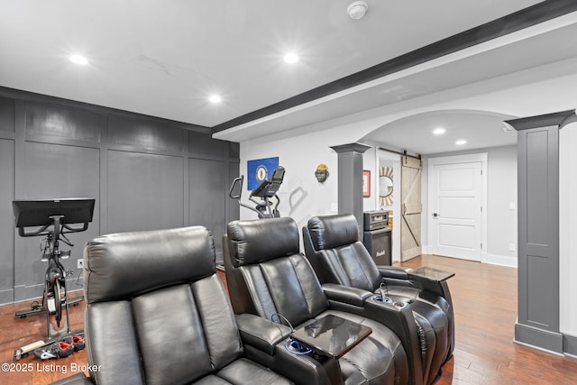 home theater featuring decorative columns, a barn door, and hardwood / wood-style floors