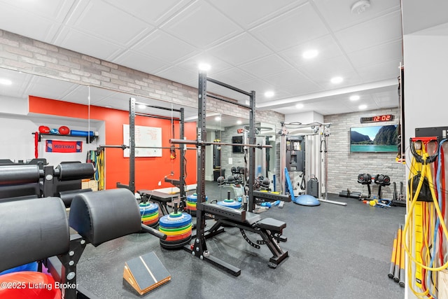 exercise room featuring brick wall and a paneled ceiling