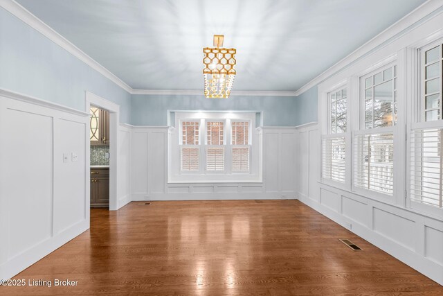 unfurnished dining area with an inviting chandelier, hardwood / wood-style flooring, and crown molding