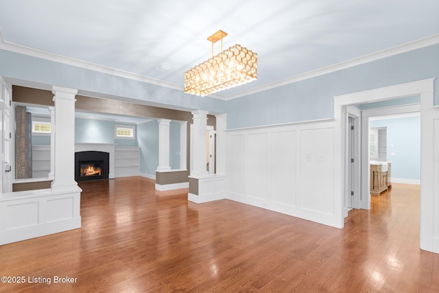 unfurnished living room featuring ornate columns, ornamental molding, and hardwood / wood-style floors