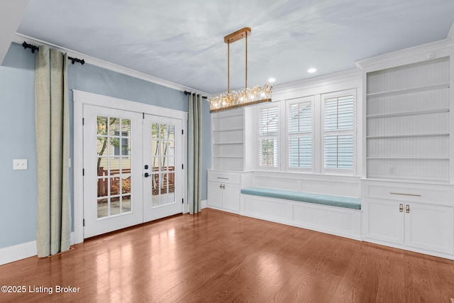 unfurnished dining area featuring french doors, wood-type flooring, crown molding, and built in shelves