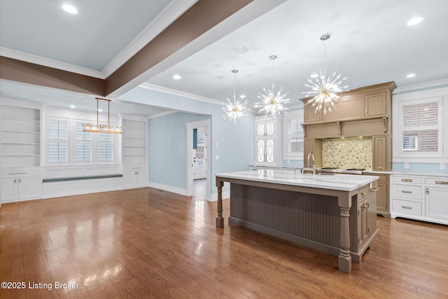 kitchen with tasteful backsplash, a center island with sink, ornamental molding, pendant lighting, and hardwood / wood-style floors