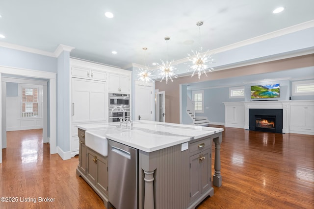 kitchen with gray cabinetry, hanging light fixtures, a center island with sink, ornamental molding, and appliances with stainless steel finishes