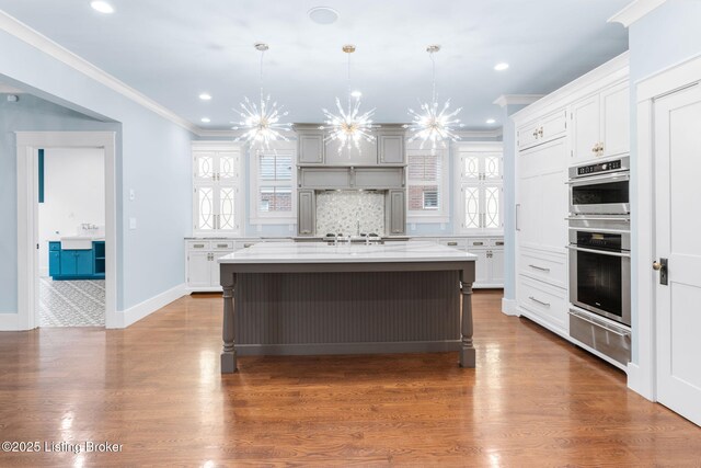 kitchen featuring double oven, an island with sink, hanging light fixtures, ornamental molding, and a notable chandelier