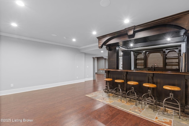 bar featuring dark wood-type flooring, crown molding, and decorative columns