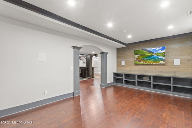 unfurnished living room with dark wood-type flooring, decorative columns, and wood walls