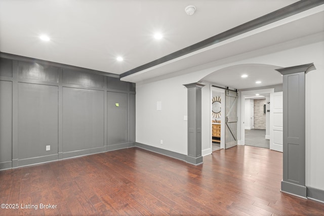 interior space featuring decorative columns, a barn door, and dark wood-type flooring