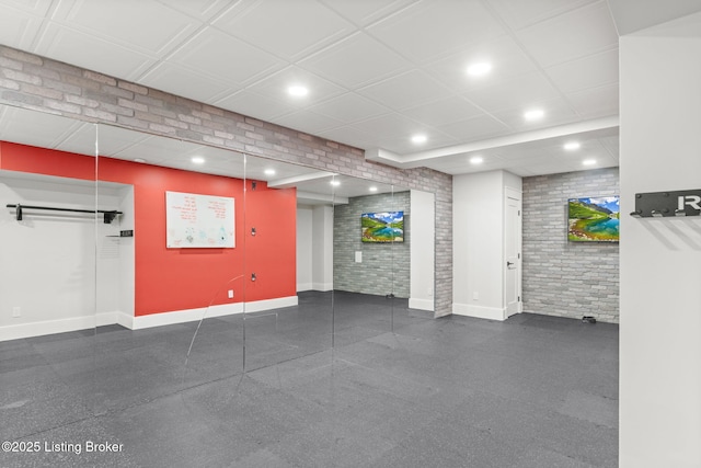 basement featuring a drop ceiling and brick wall