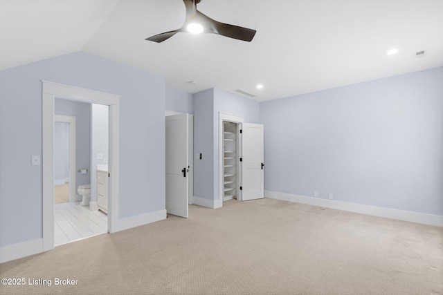 unfurnished bedroom with ceiling fan, ensuite bathroom, a spacious closet, vaulted ceiling, and light colored carpet