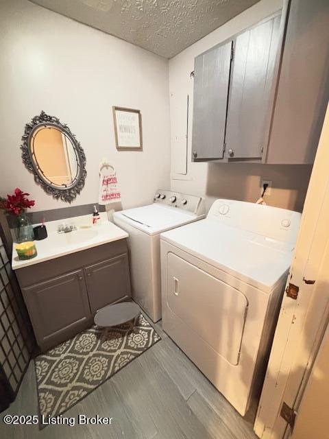 laundry room featuring cabinets, a textured ceiling, washer and clothes dryer, sink, and hardwood / wood-style flooring