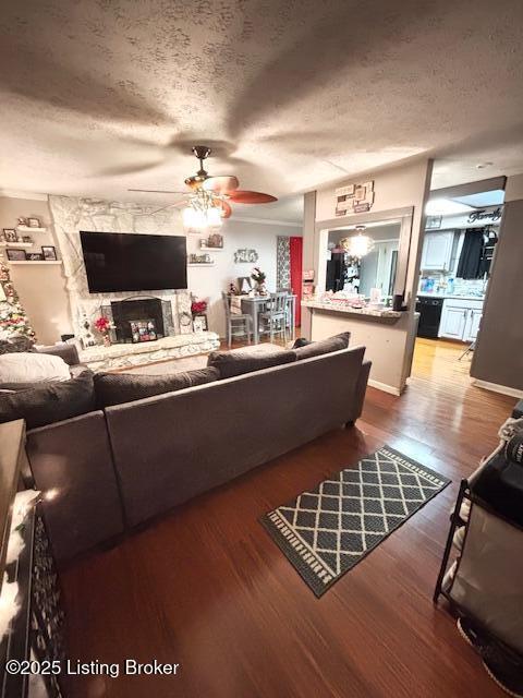 living room with a textured ceiling, ceiling fan, a fireplace, and hardwood / wood-style floors