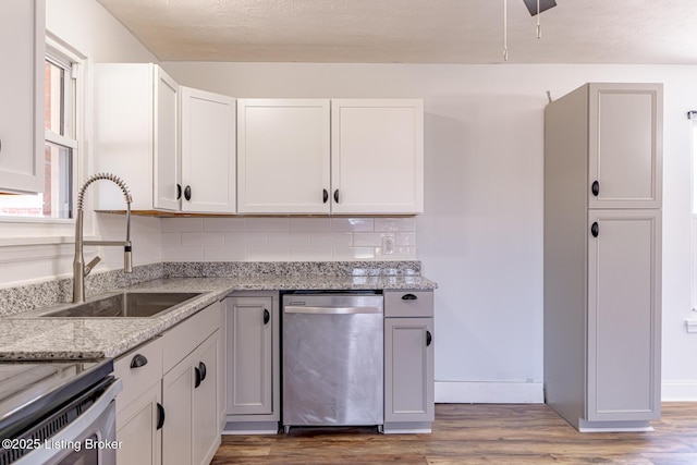 kitchen with white cabinets, sink, stainless steel dishwasher, tasteful backsplash, and light stone counters