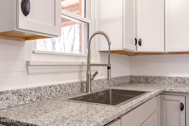 kitchen with white cabinets, backsplash, light stone counters, and sink