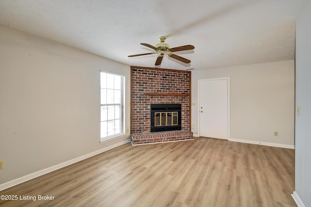 unfurnished living room with ceiling fan, a textured ceiling, a brick fireplace, and light hardwood / wood-style flooring