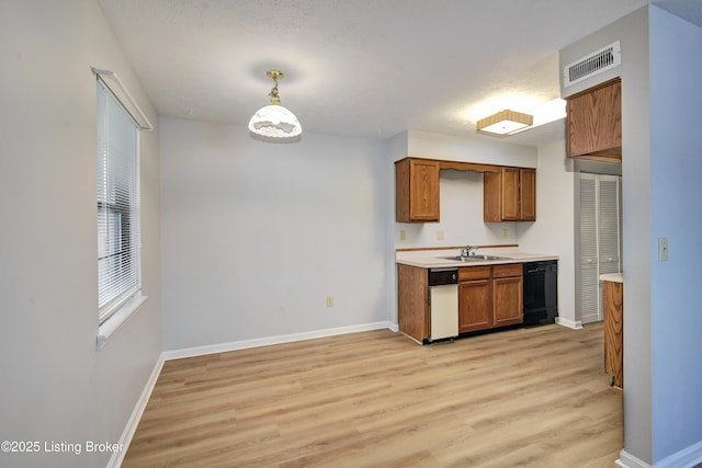 kitchen featuring hanging light fixtures, sink, black dishwasher, and light wood-type flooring