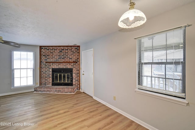 unfurnished living room featuring a brick fireplace, light hardwood / wood-style flooring, and a textured ceiling