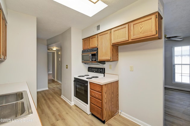 kitchen with sink, electric range, a skylight, light hardwood / wood-style floors, and a textured ceiling