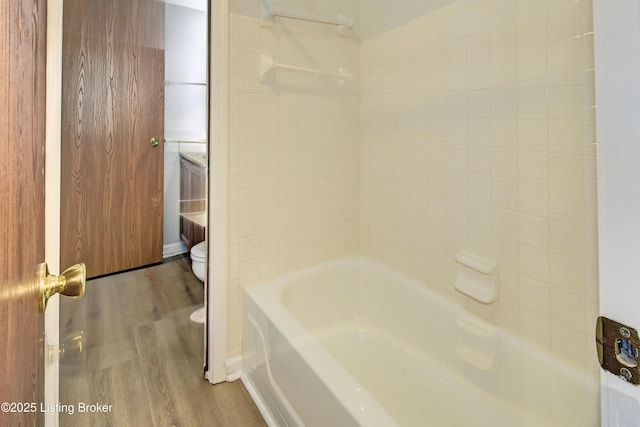 bathroom with wood-type flooring, tiled shower / bath, and toilet