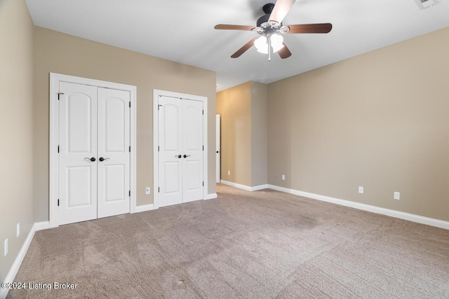 unfurnished bedroom featuring carpet, ceiling fan, and multiple closets