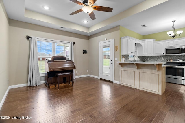 kitchen with white cabinetry, a tray ceiling, decorative backsplash, a breakfast bar, and appliances with stainless steel finishes