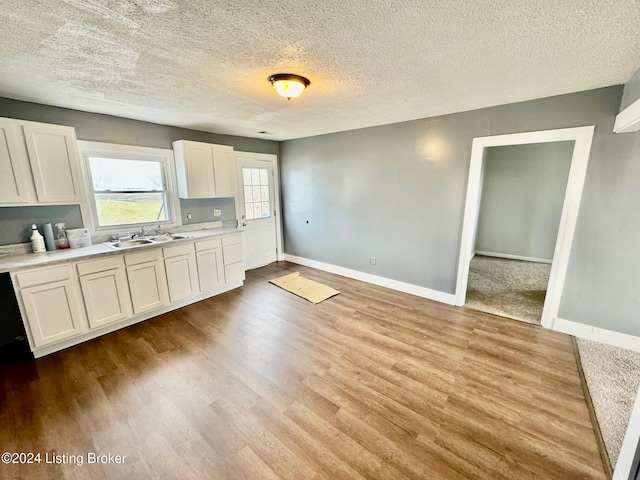 kitchen with a textured ceiling, light hardwood / wood-style flooring, white cabinetry, and sink