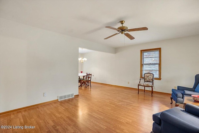 living area with ceiling fan with notable chandelier and light hardwood / wood-style flooring