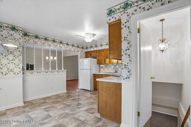 kitchen featuring sink, hanging light fixtures, ceiling fan with notable chandelier, and white refrigerator