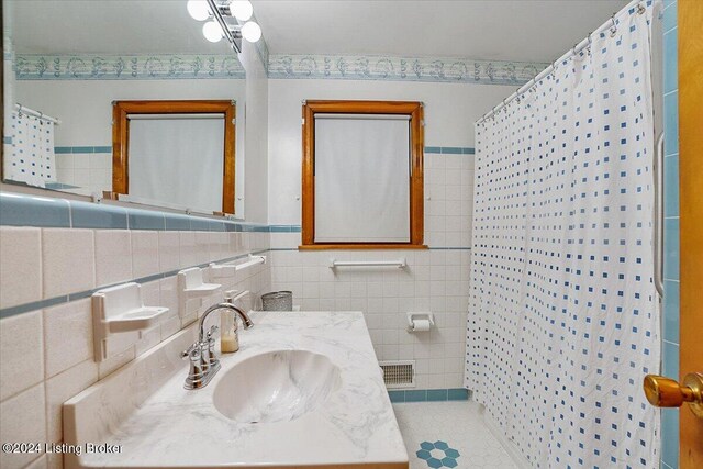 bathroom with walk in shower, vanity, tile patterned flooring, and tile walls