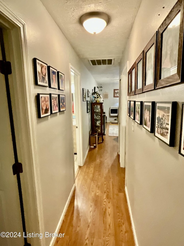 hallway with a textured ceiling and light wood-type flooring