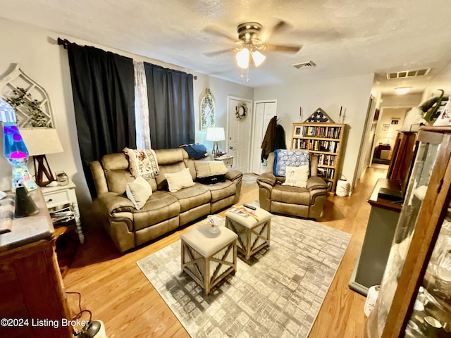 living room featuring ceiling fan, light hardwood / wood-style floors, and a textured ceiling