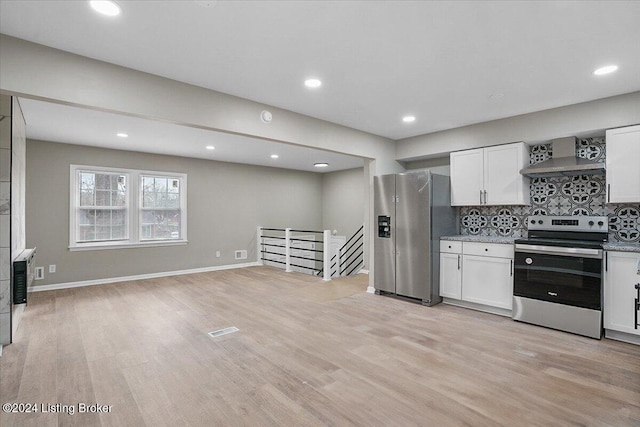 kitchen with appliances with stainless steel finishes, light wood-type flooring, white cabinetry, and wall chimney range hood