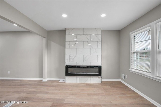 unfurnished living room with a tiled fireplace and light hardwood / wood-style floors