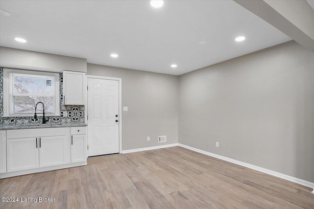 kitchen with light stone counters, light wood-type flooring, white cabinetry, and sink