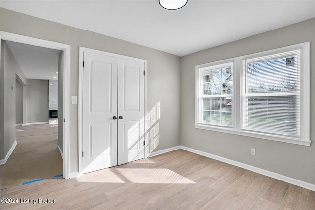 unfurnished bedroom featuring a large fireplace, a closet, and light wood-type flooring