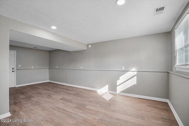 empty room with a textured ceiling and light hardwood / wood-style flooring