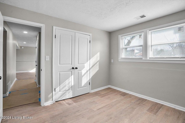 unfurnished bedroom featuring light wood-type flooring, a textured ceiling, and a closet