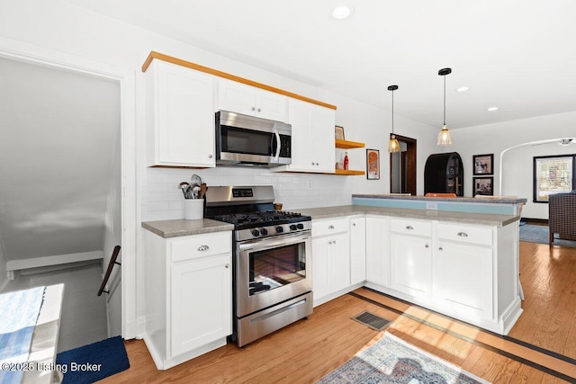 kitchen featuring decorative light fixtures, white cabinetry, tasteful backsplash, kitchen peninsula, and appliances with stainless steel finishes