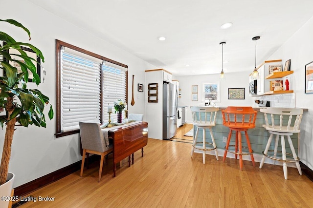 kitchen with pendant lighting, stainless steel appliances, light wood-type flooring, white cabinetry, and a kitchen breakfast bar