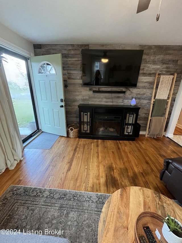 living room with ceiling fan, wood walls, and wood-type flooring